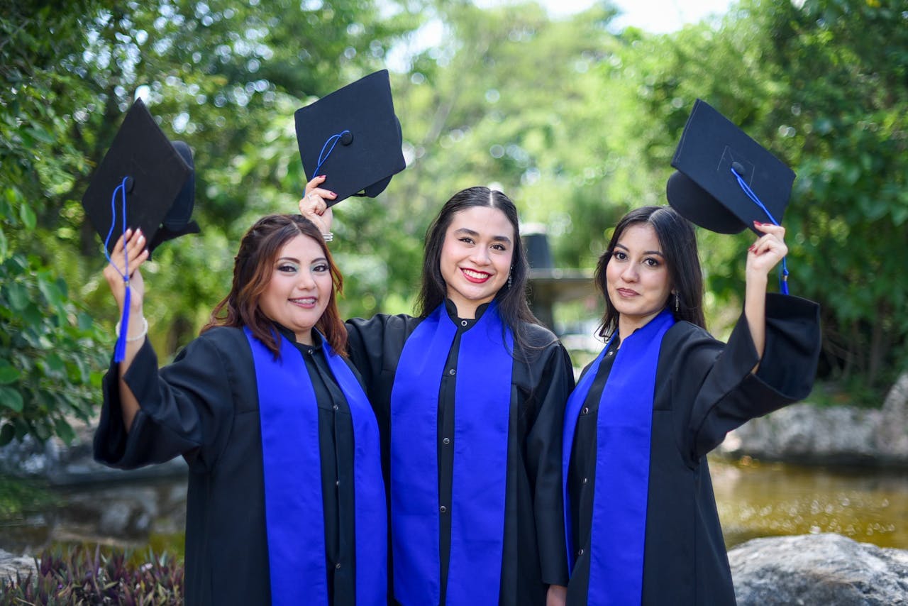 Three female graduates in gowns and caps celebrating outdoors, showing achievement and joy.